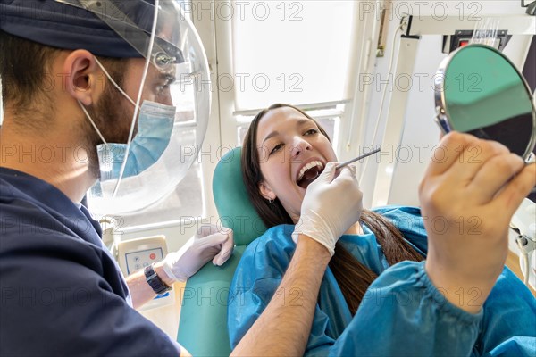 Young dentist in mask examining teeth of female Young dentist with mask and female patient in dental office