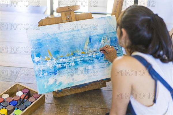 Woman artist painting on a canvas a blue abstract painting. Creative ywoman working on the floor in her art studio