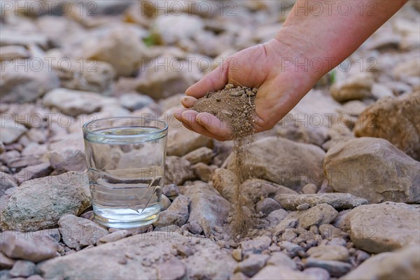 Woman's hand with dry earth next to a glass of crystal clear water in a dry river bed