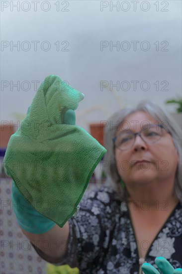 Closeup of a woman cleaning the windows of her house with a green rag and rubber gloves