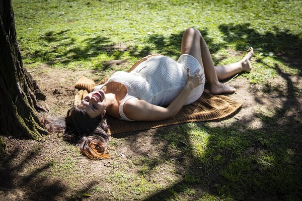 Pregnant Latina woman lying on the grass in a park