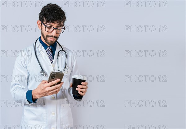 Young doctor holding a coffee to go and phone. Doctor with phone and holding coffee to go