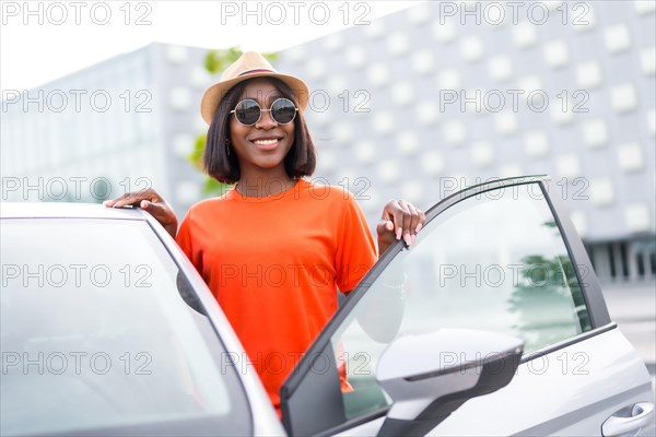 Stylish summer: black woman in orange shirt and sunglasses opening car door with a smile
