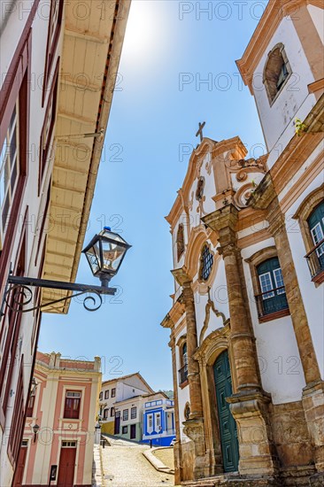 18th century baroque church seen from below with surrounding colonial style houses and cobblestone slope in the background in the historic town of Ouro Preto