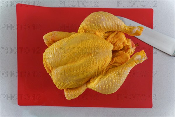 Top view of a peeled free-range chicken on a red board with a knife
