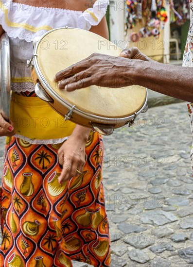Tambourine player with a woman in typical clothes dancing in the background in the streets of the Pelourinho district in Salvador