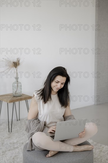 Young woman sitting comfortably with laptop on a stool in the living room