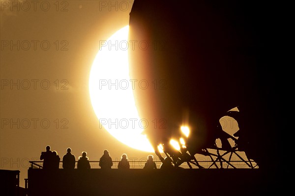 The silhouettes of people and the former listening station on Teufelsberg stand out against the setting sun in Berlin