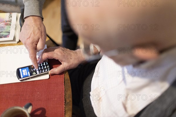 Son explains to demented father how to use a senior citizen's mobile phone.