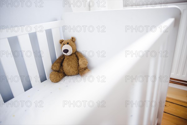 Symbolic photo on the subject of wanting a child. A teddy bear sits in an empty cot. Berlin