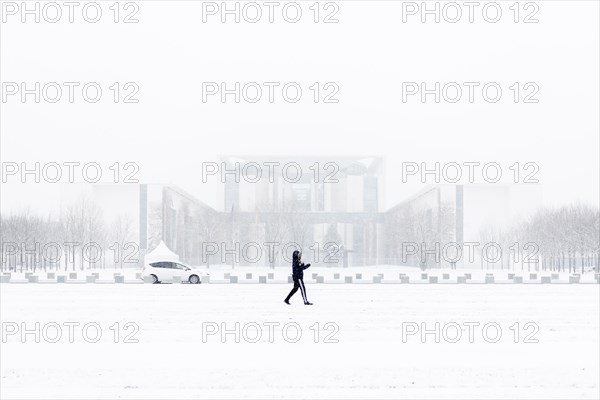 A person is silhouetted in front of the Chancellery in the driving snow in Berlin