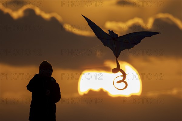 A silhouette of a child flying a kite in front of the sunset in Berlin