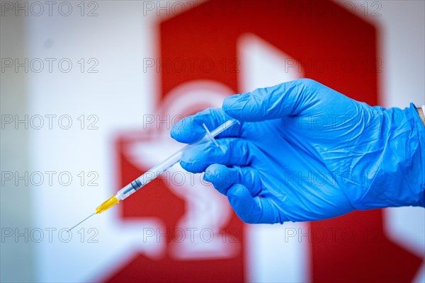 A pharmacist holding a syringe in front of a pharmacy logo in a pharmacy in Duesseldorf