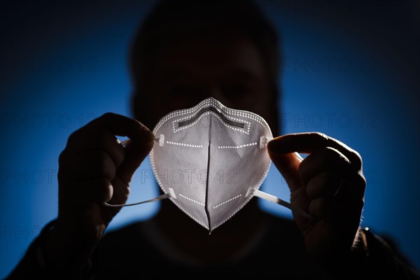 A man holds an FFP2 protective mask in front of his face. Berlin