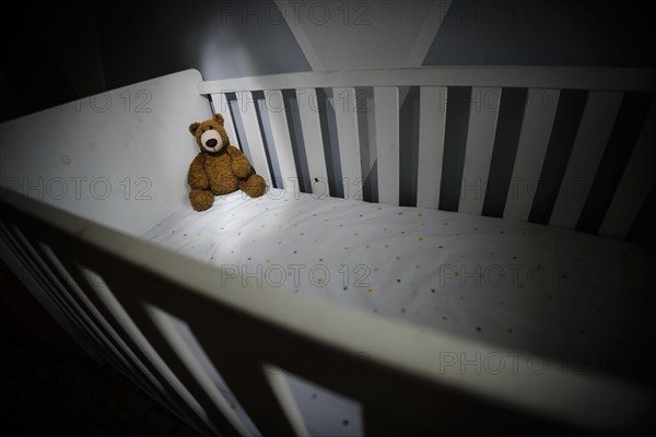 Symbolic photo on the subject of child abuse. A teddy bear sits in an empty cot. Berlin