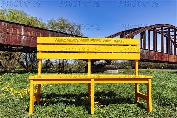 Oversized yellow wooden bench in front of old railway bridge