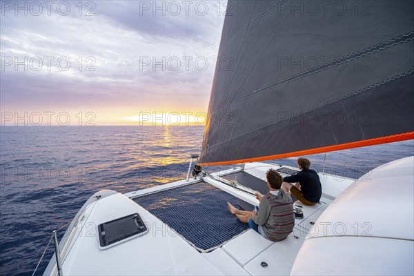 Two young men sitting on catamaran looking into the sunset