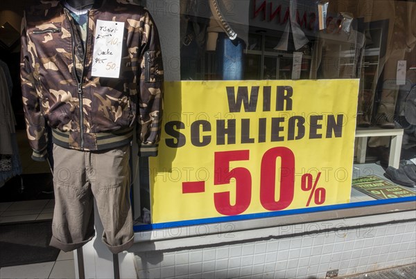 Sign with 50 percent discount due to business closure at the window of a clothing shop in the pedestrian zone