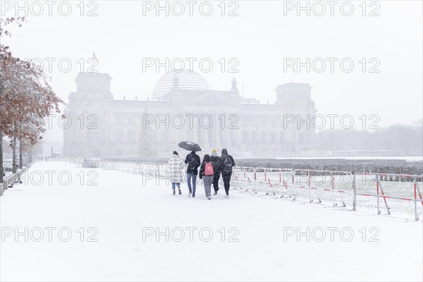 Five people stand in front of the Bundestag in the driving snow in Berlin