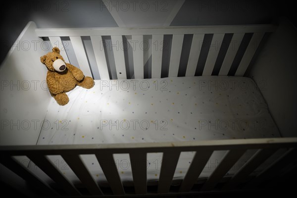 Symbolic photo on the subject of child abuse. A teddy bear sits in an empty cot. Berlin