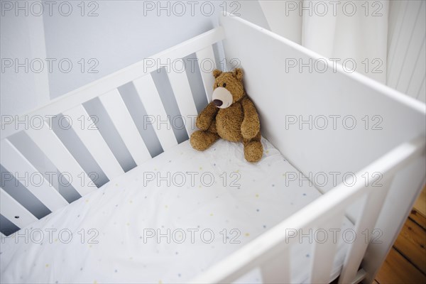 Symbolic photo on the subject of wanting a child. A teddy bear sits in an empty cot. Berlin