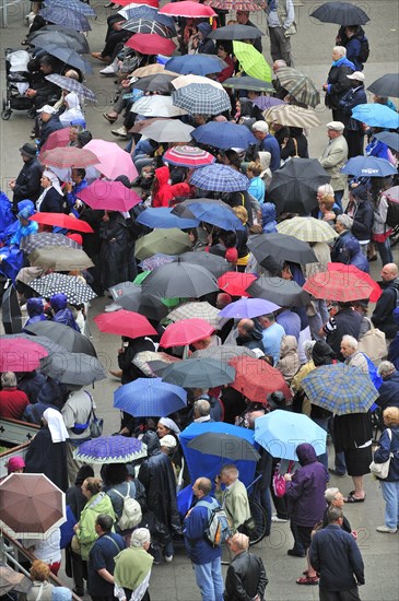 Pilgrims with umbrellas in the rain praying in front of the grotto at the Sanctuary of Our Lady of Lourdes