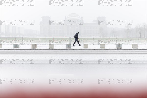 A person stands in front of the Bundestag in the driving snow in Berlin