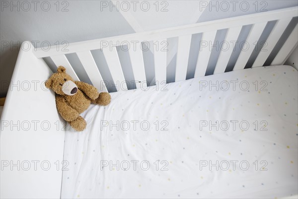 Symbolic photo on the subject of wanting a child. A teddy bear sits in an empty cot. Berlin