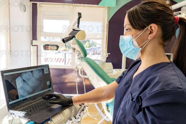 Young doctor wearing a mask watches an X-ray on the computer in her dental office