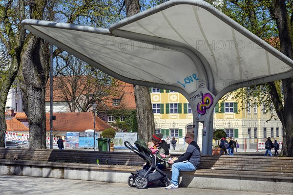 Rain and sun protection over park bench and parents with pram