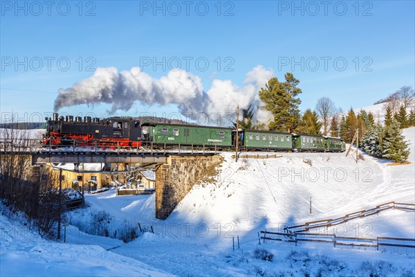Steam train of the Fichtelbergbahn railway Steam locomotive on a bridge in winter in Sehmatal