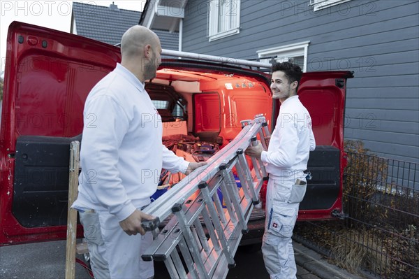 Subject: Master painter and apprentice loading a van with work materials