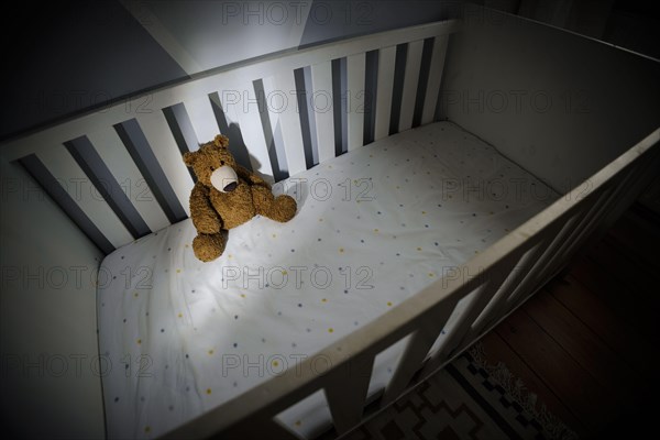 Symbolic photo on the subject of child abuse. A teddy bear sits in an empty cot. Berlin