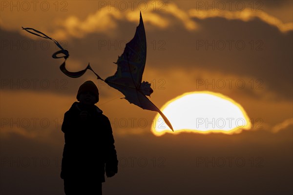 A silhouette of a child flying a kite in front of the sunset in Berlin