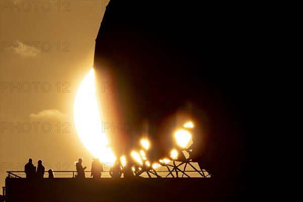 The silhouettes of people and the former listening station on Teufelsberg stand out against the setting sun in Berlin