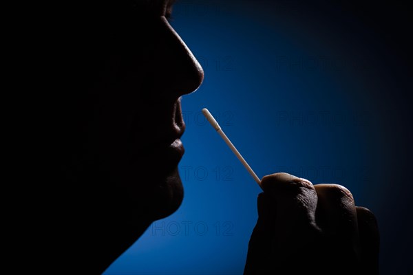 A man holds cotton swabs of a Sars-COV-2 Rapid Antigen Test to his nose. Berlin