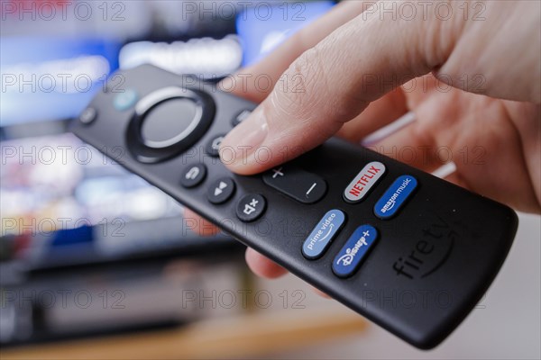 The remote control of an Amazon Fire TV Stick is held in front of a television. Berlin