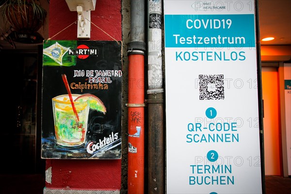 A board of a bar advertising Caipirinha cocktails stands next to the sign of a Covid-19 test centre in the old town of Duesseldorf