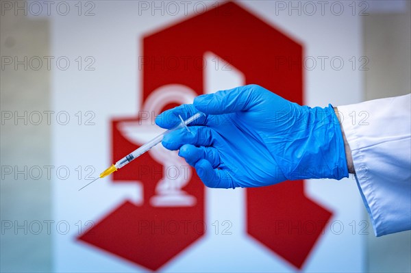 A pharmacist holding a syringe in front of a pharmacy logo in a pharmacy in Duesseldorf