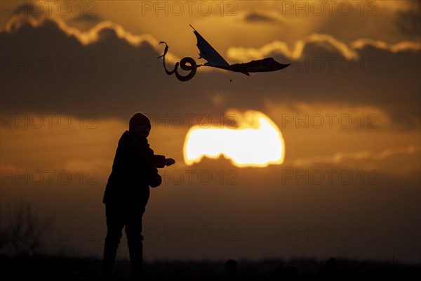 A silhouette of a child flying a kite in front of the sunset in Berlin