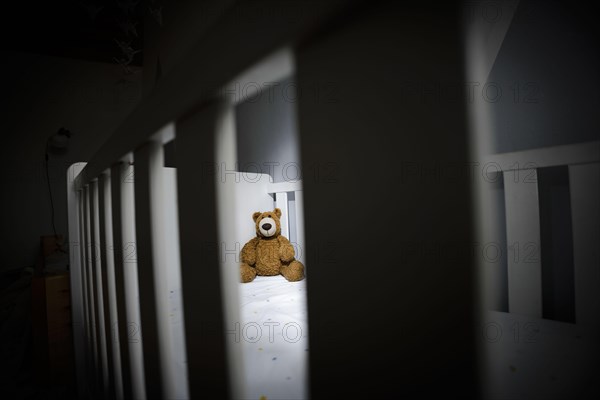 Symbolic photo on the subject of child abuse. A teddy bear sits in an empty cot. Berlin