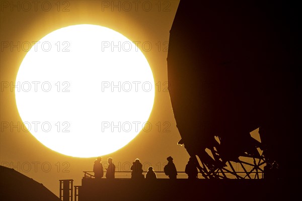 The silhouettes of people and the former listening station on Teufelsberg stand out against the setting sun in Berlin