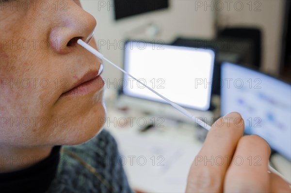 Symbol photo on the subject of ' Compulsory testing in the office'. A woman swabs her nose for a Sars Covid-19 antigen rapid test in front of her desk. Berlin