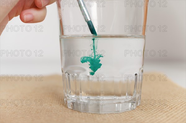Close-up of a glass of water with a woman's hand dipping a watercolor brush in it