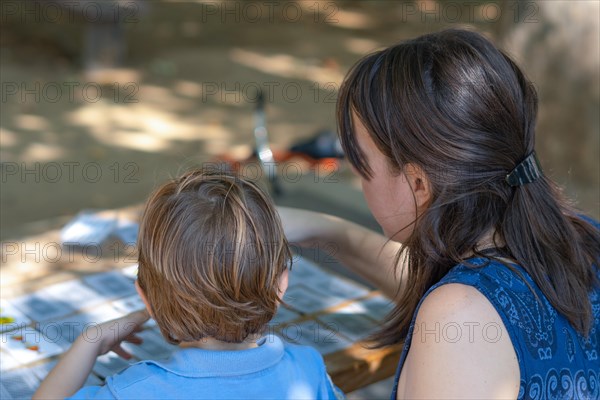 Rear view of a young mother teaching her son to play cards at a park table