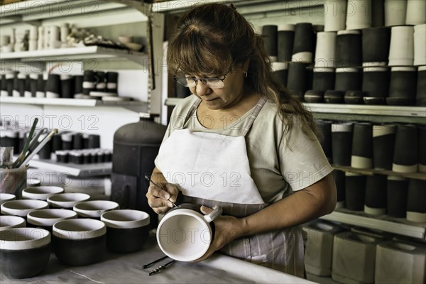 Middle-aged woman craftswoman with apron making the sgraffito on a piece of pottery