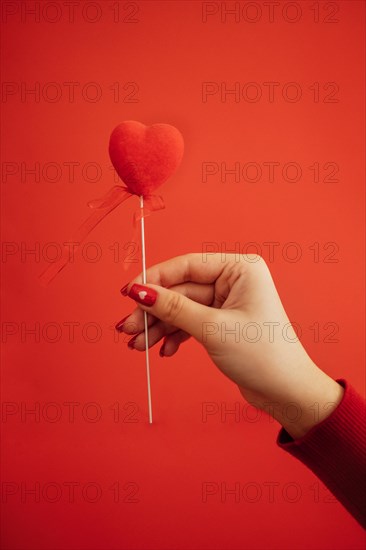 Decorative heart on a stick with ribbon in hand of the woman. Bright background with silver sequins and round confetti. Sovereign velvet hearts on a red backdrop. Copy space. Valentine day concept