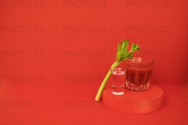 A glass of red cocktail with greens on the podium. Stylish alcohol tomato beverage Bloody Mary on a red background. Delicious drinks concept. Copy space