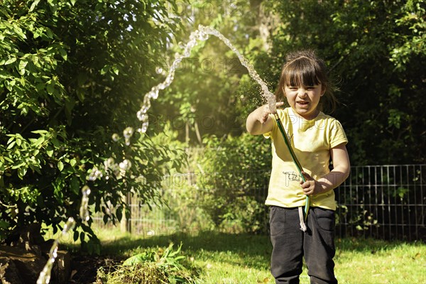 Happy little girl playing with a garden hose. Preschool child having fun with watering trees and plants in domestic garden