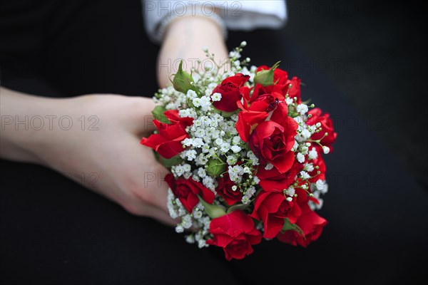 Two hands hold a small bouquet of red roses